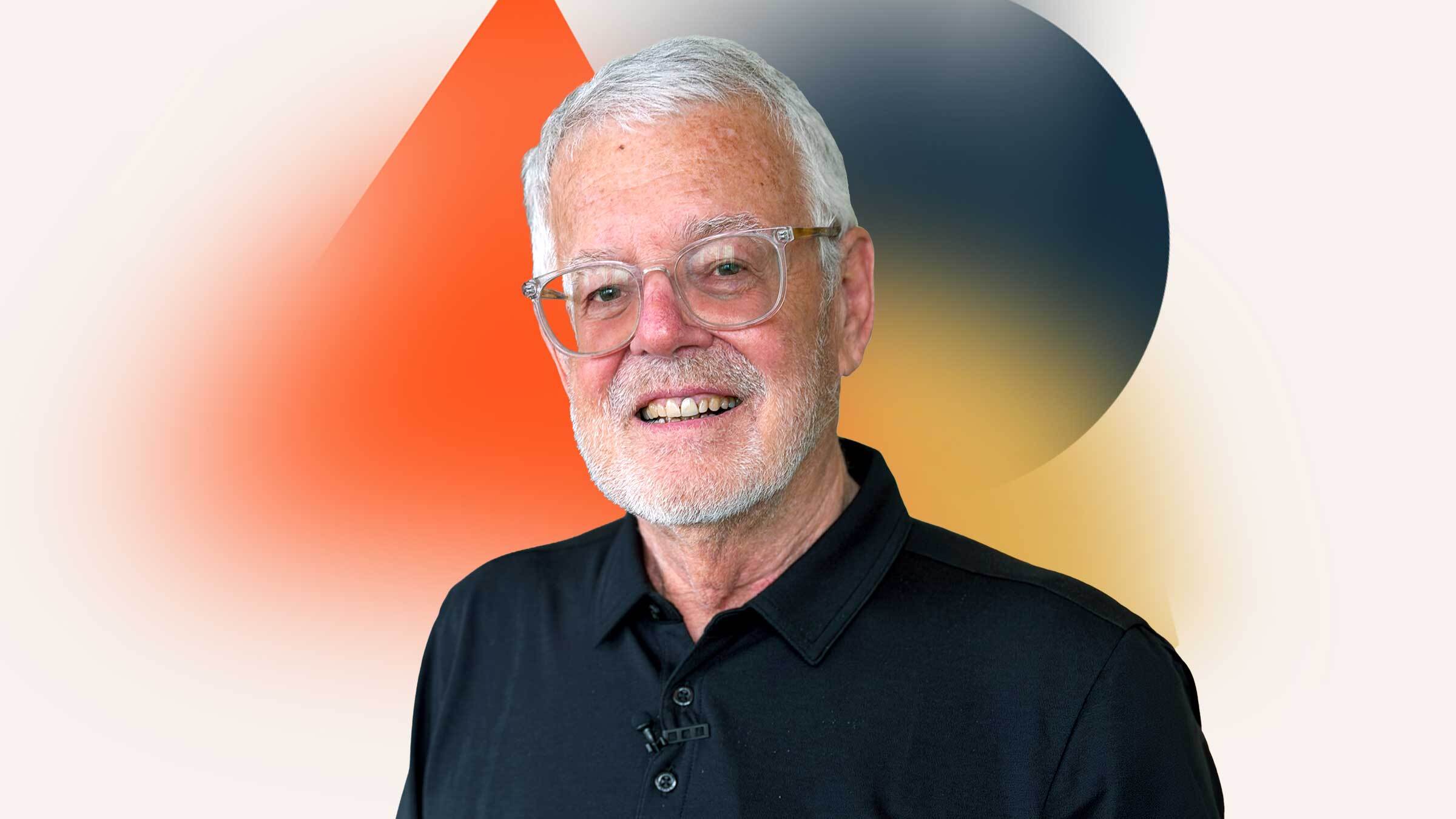Portrait of a man with white hair and short cropped beard, wearing glasses and a dark shirt.