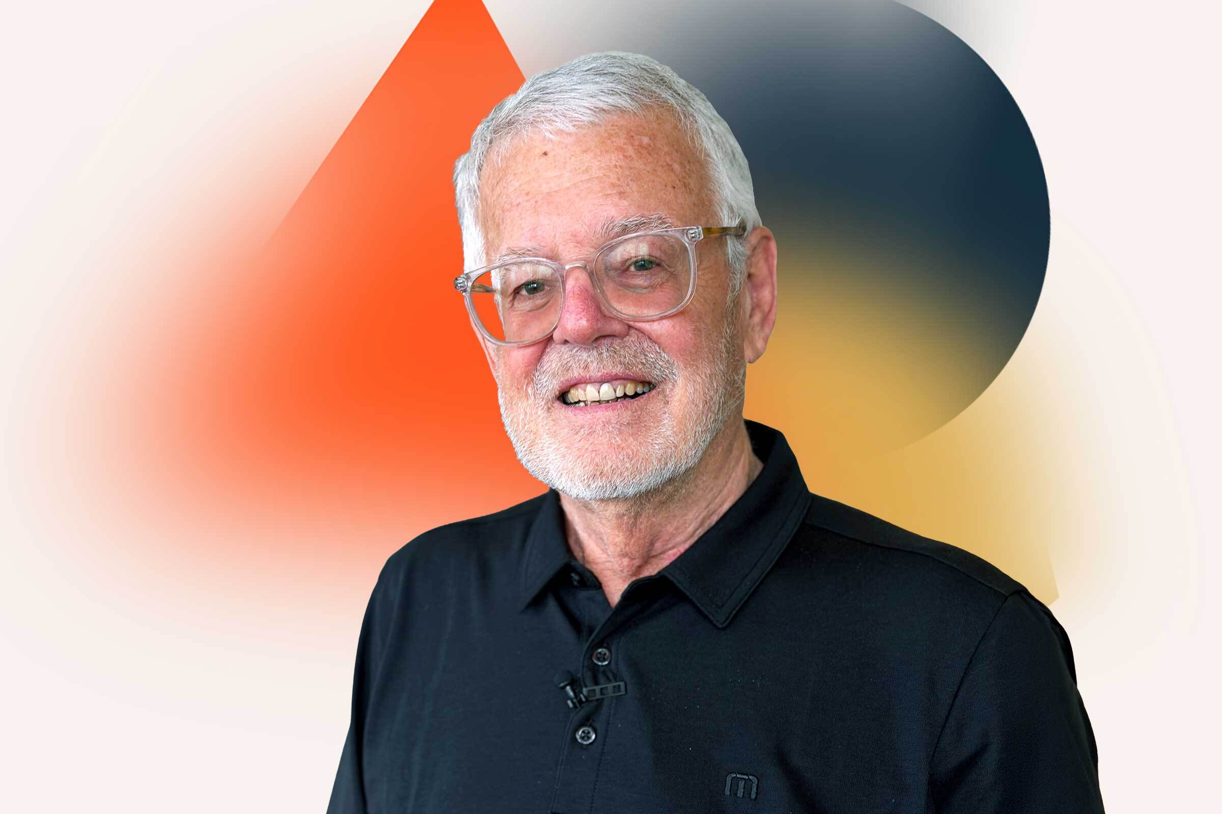Portrait of a man with white hair and short cropped beard, wearing glasses and a dark shirt.