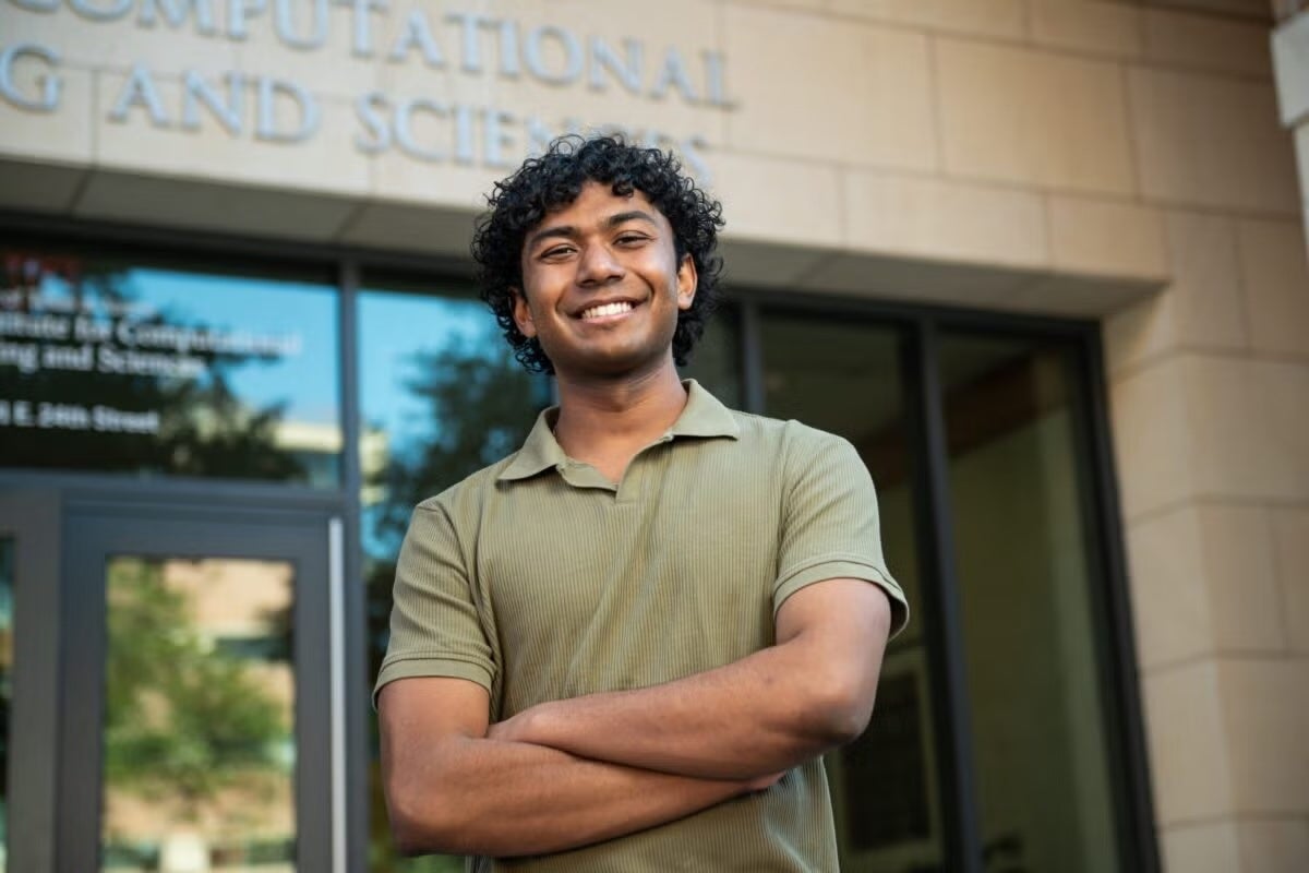 A young man in a polo-style shirt crosses his arms and smiles standing before a limestone building labeled computational engineering and sciences. 