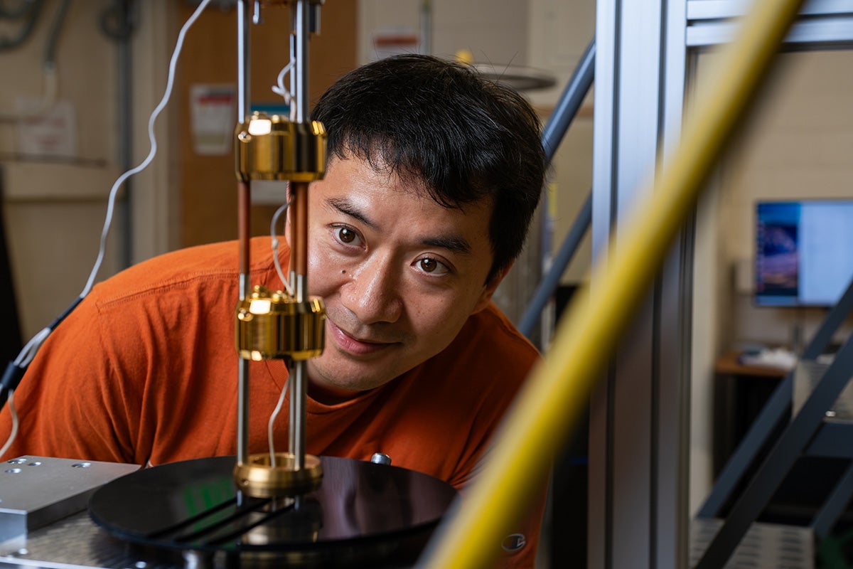A scientist wearing an orange shirt bends over to look at a piece of scientific equipment