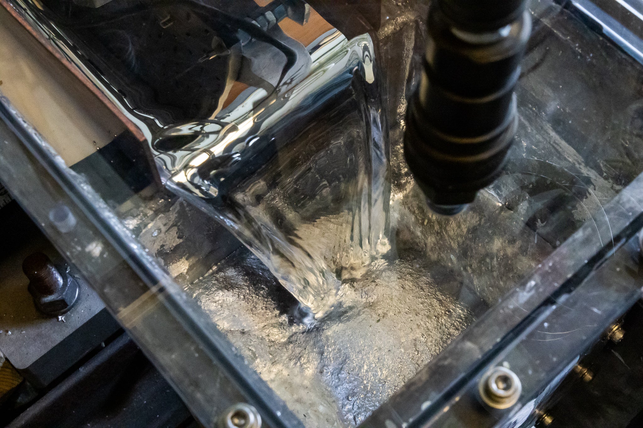 Metalic looking fluid pours out of a channel and into a lower reservoir