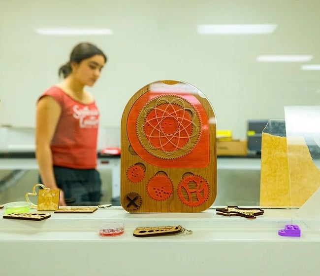 A young woman walks behind a shelf of colorful tchotchkes and inventions of varying sizes.