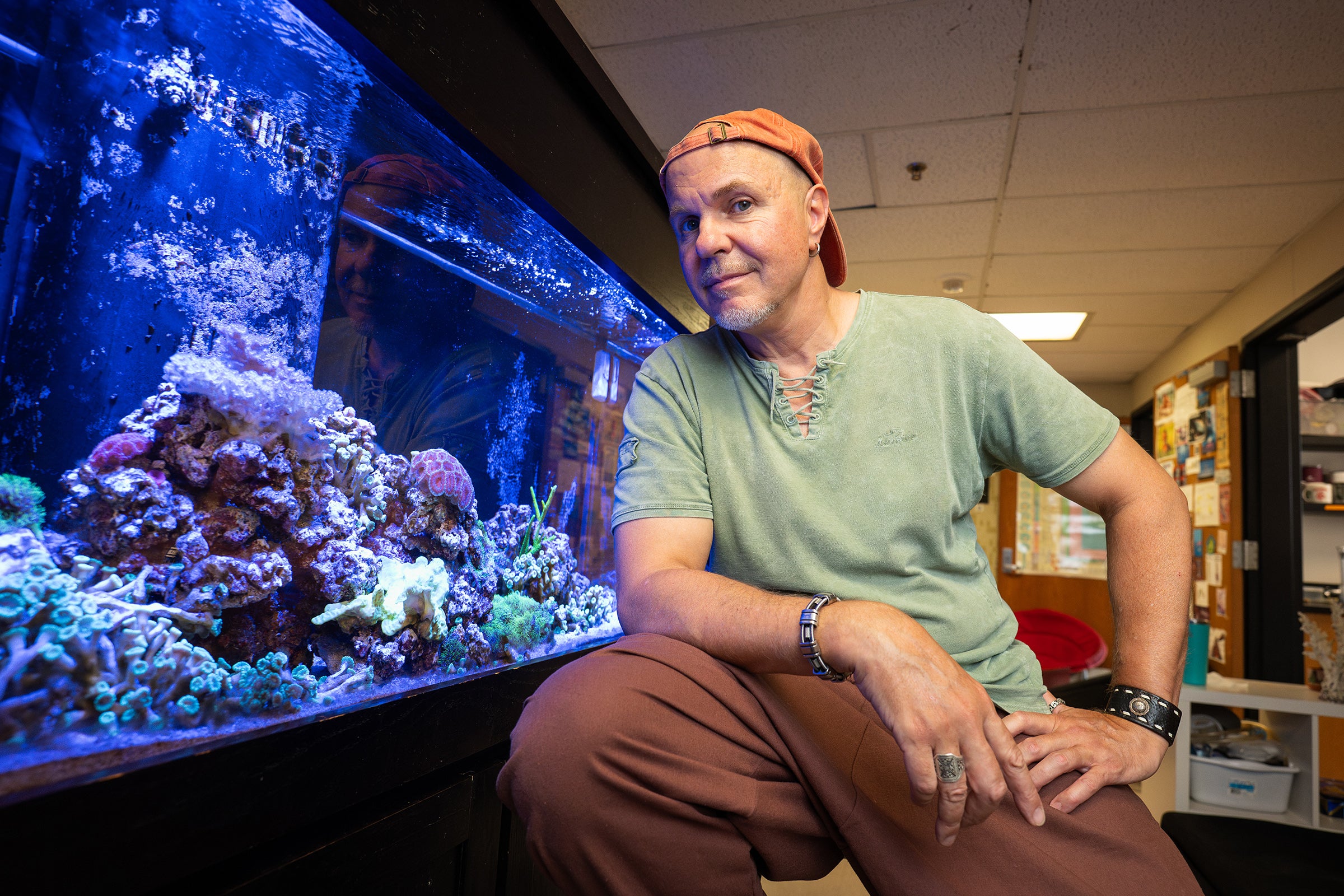 A man sits next to an aquarium with corals.
