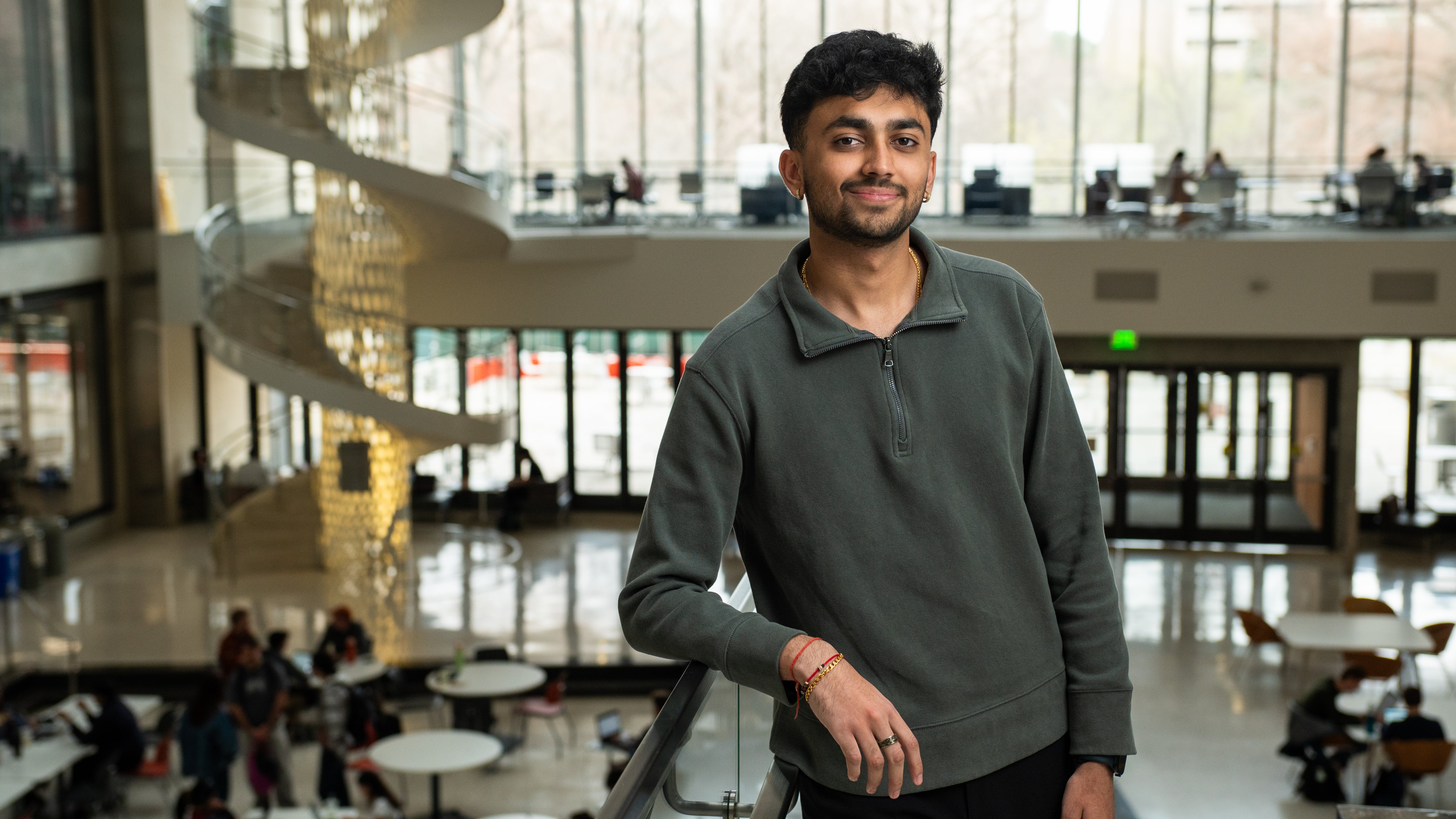 Portrait of a male student with short dark hair standing in a large atrium with natural light