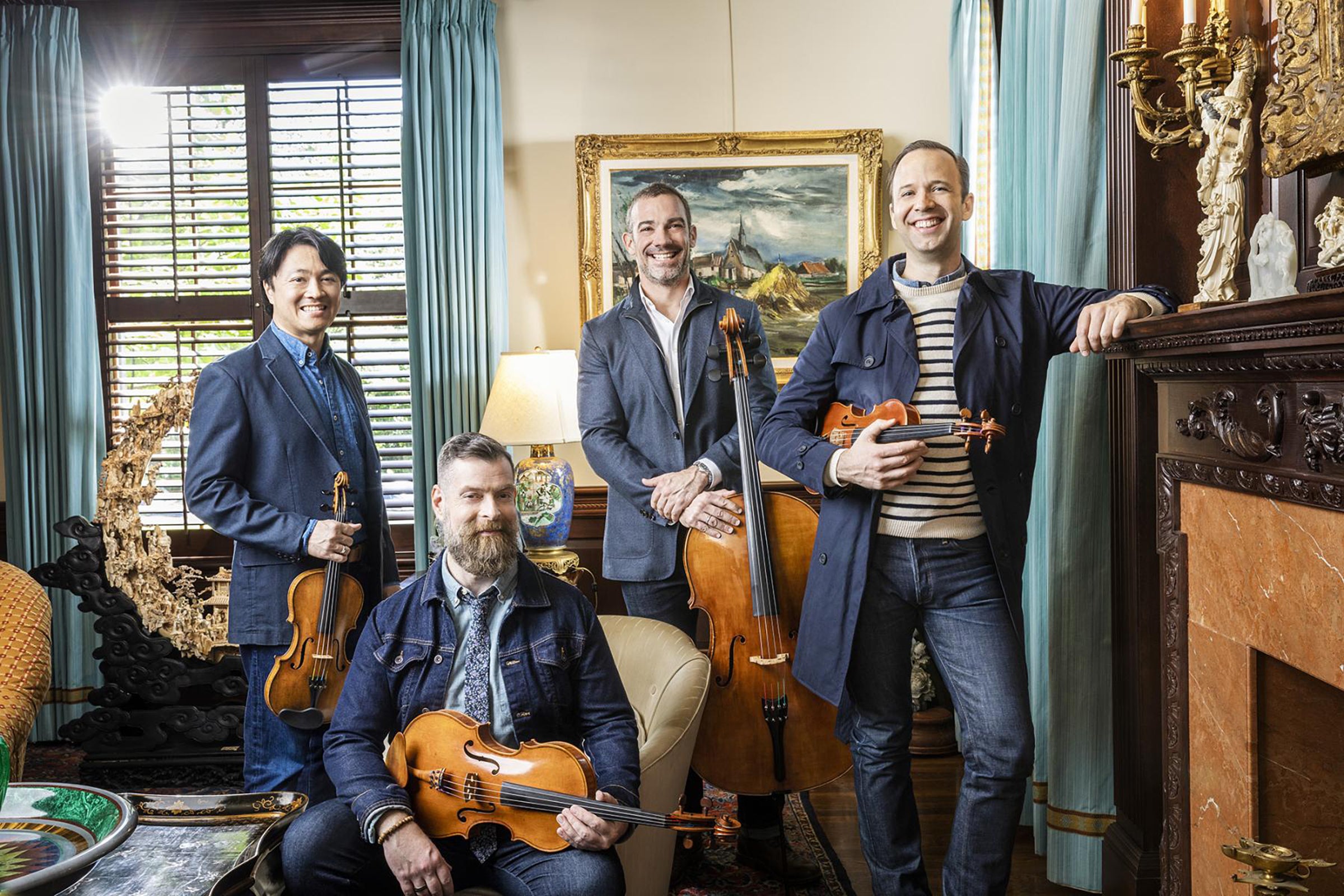 The Miró Quartet posing with their instruments in front of a fireplace.