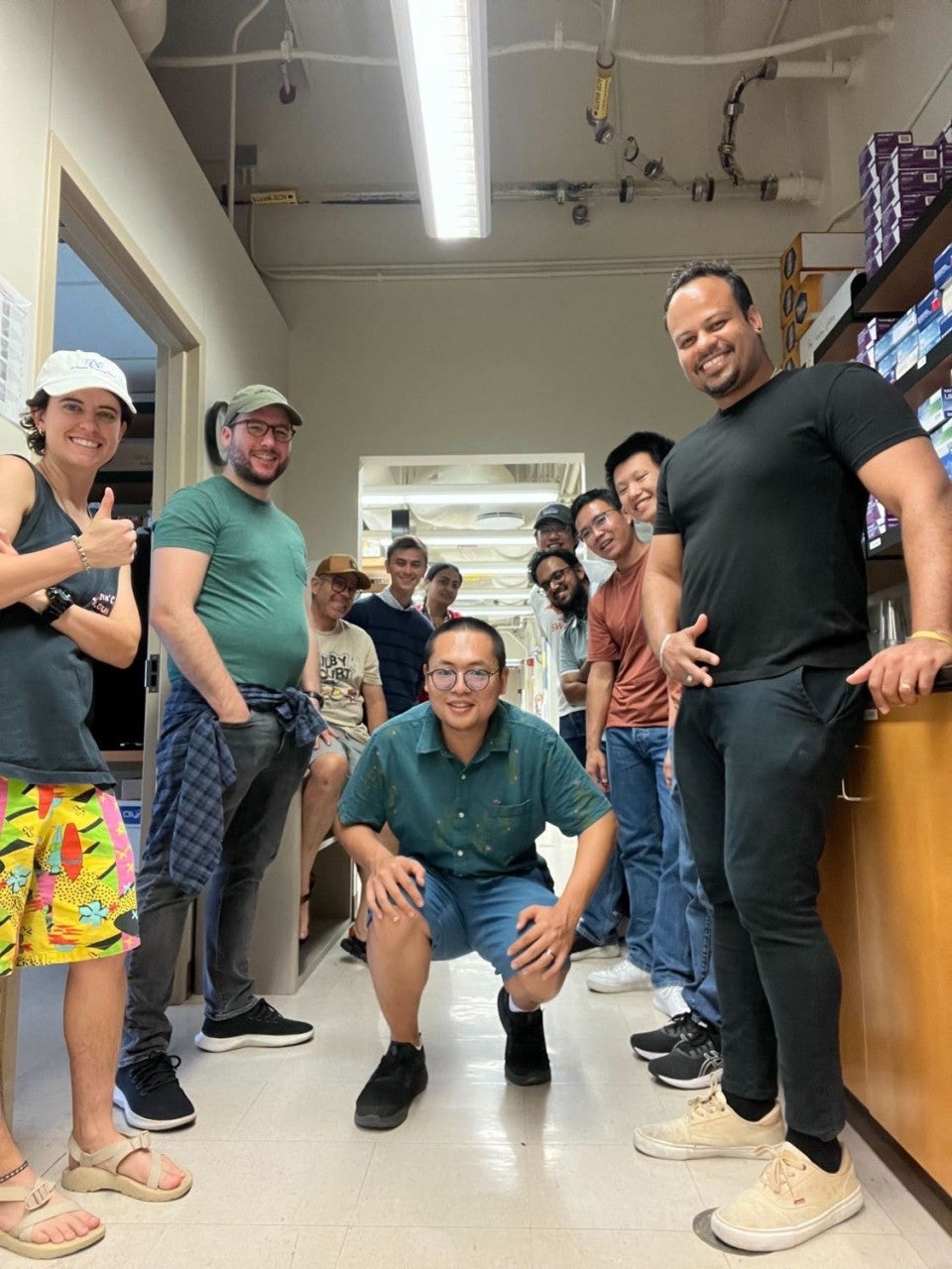 A young man squats in the middle while several others in casual clothes surround him for a group shot in a lab area.