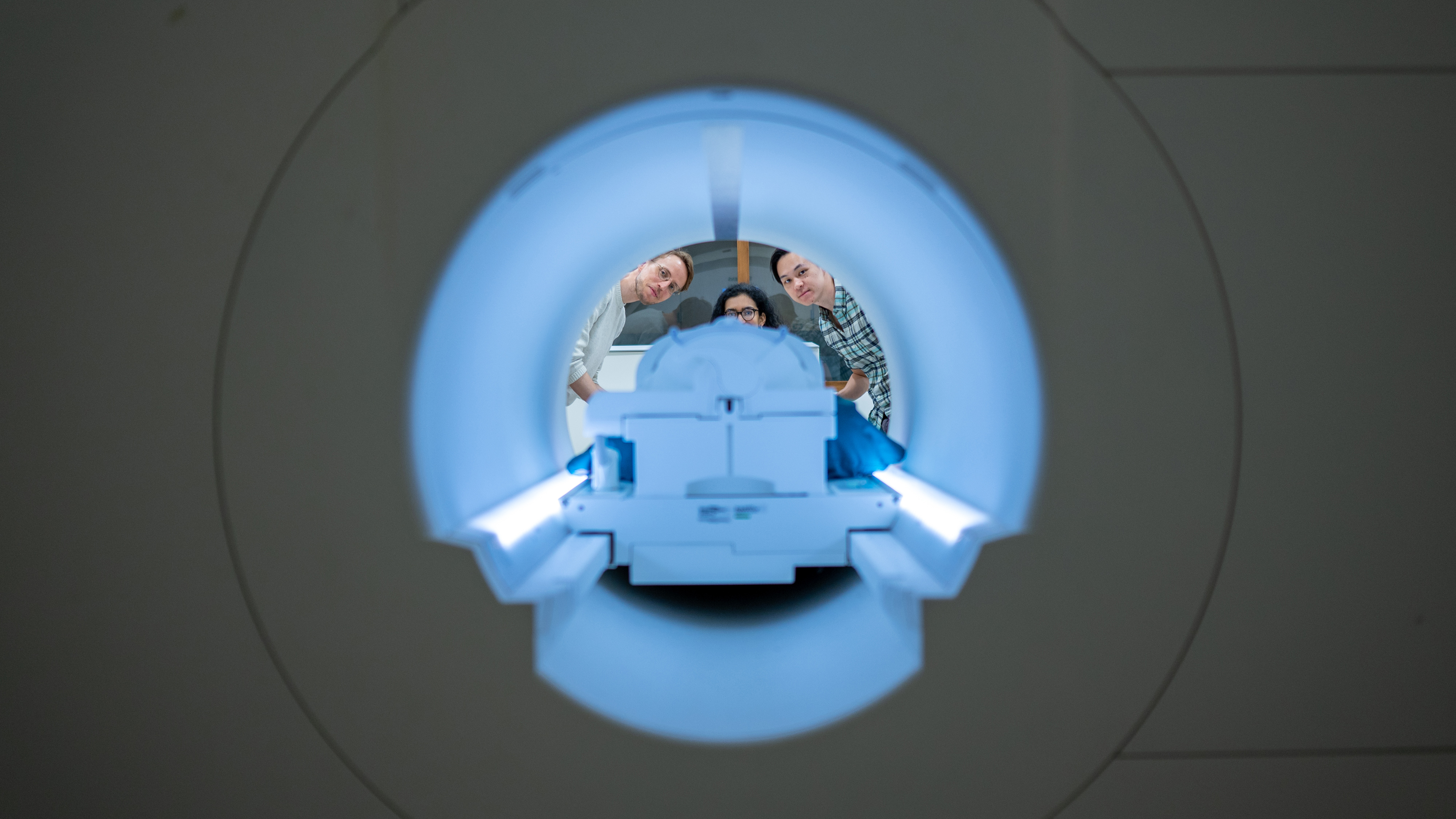 Three researchers peer inside an MRI machine