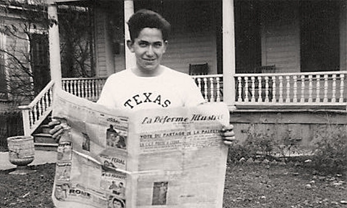 A young man in a Texas t-shirt reads a newspaper many decades ago