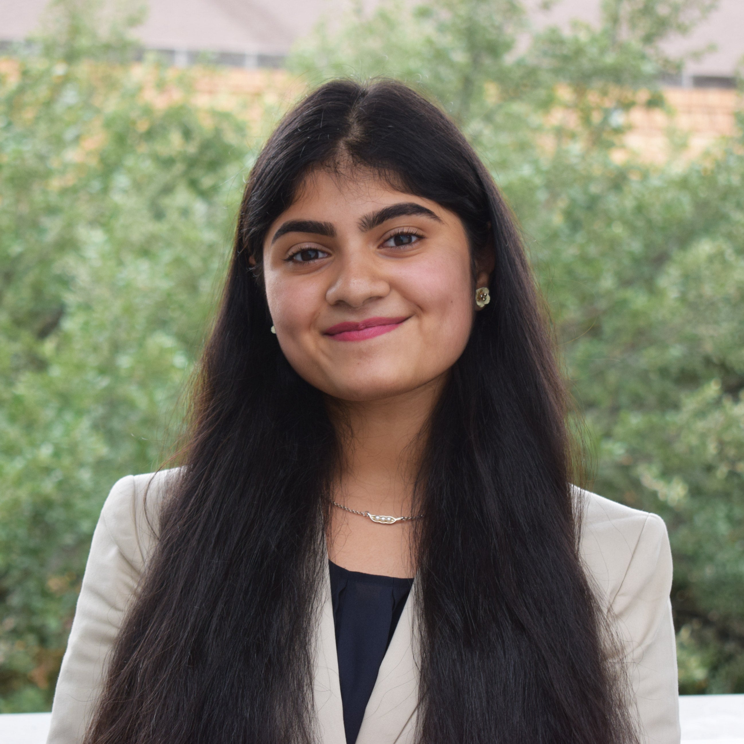 Neha Yawalkar in jacket in front of outdoor building and foliage