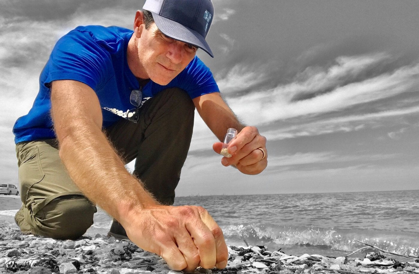 Jace Tunnell of the Nurdle Patrol on the beach crouches and picks up plastic pellets to add to a tube