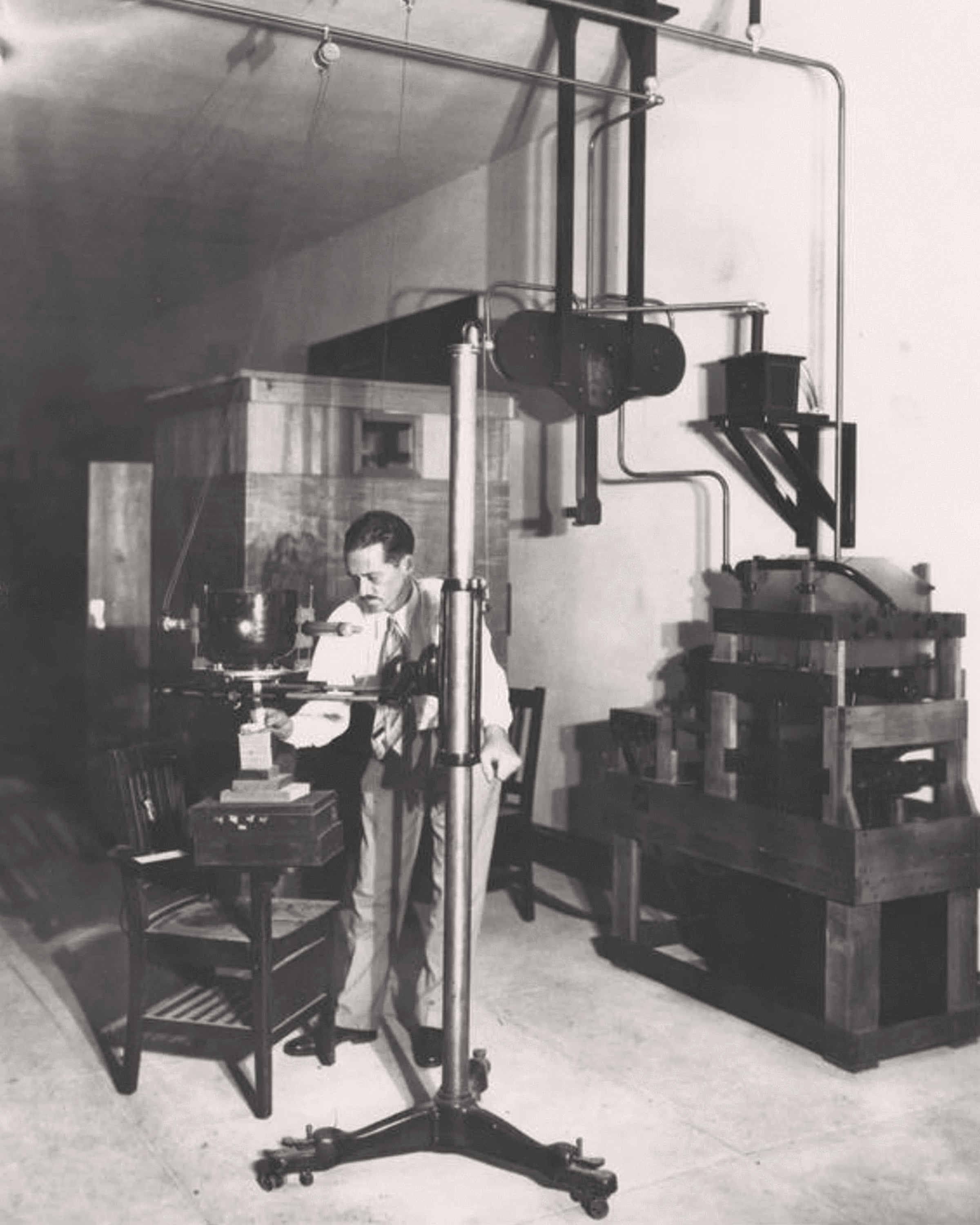 Black and white photo of a man standing next to scientific equipment in a lab