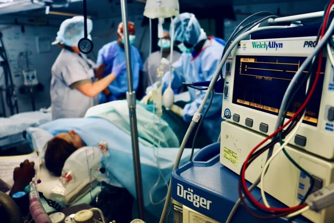 A patient lies on an operating table as a team of surgeons and health professionals discuss something.