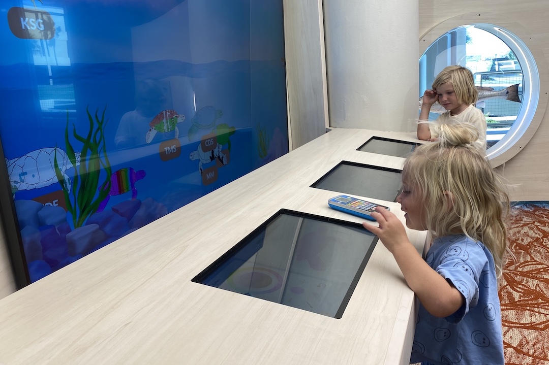 Two young children play at an exhibit that shows underwater sea life on a screen