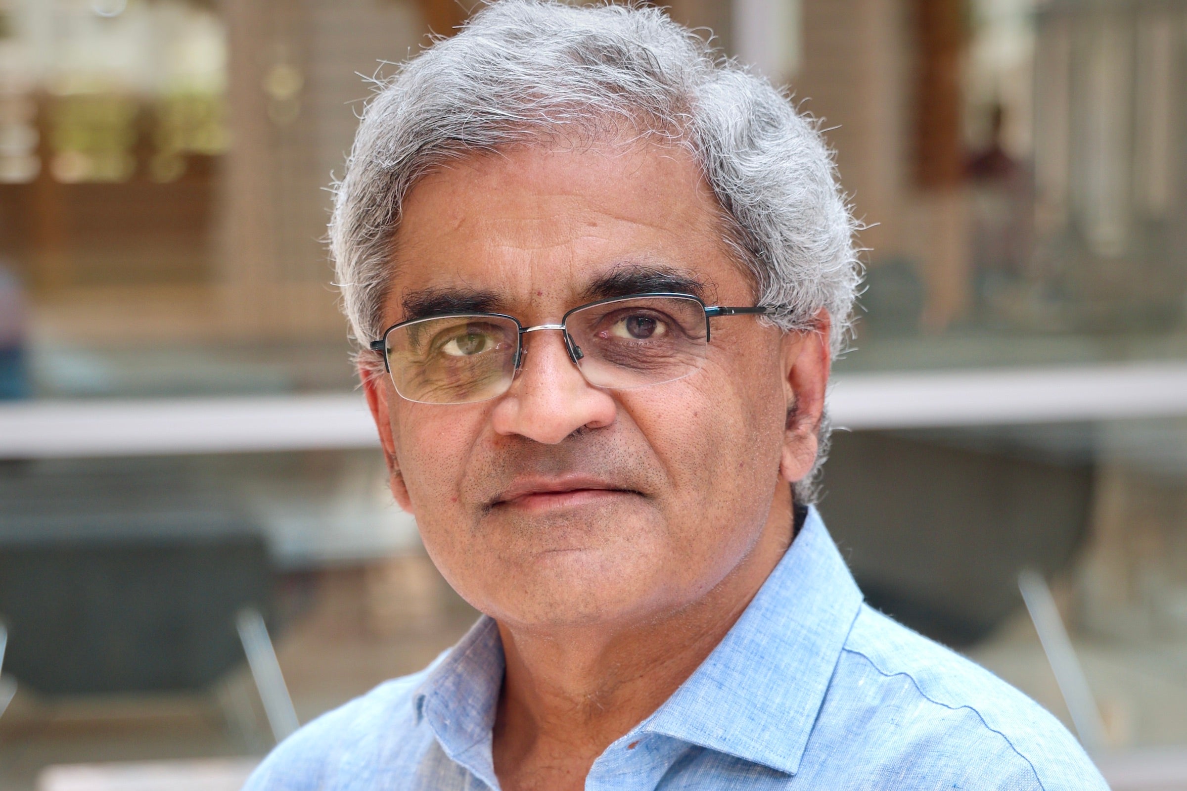 A man in a collared shirt and glasses in a building with chairs and glass behind him