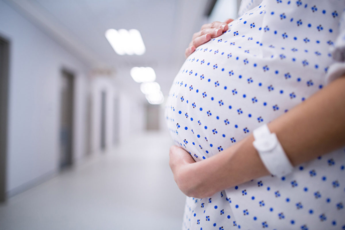 Hands hold a pregnant belly in a hospital gown in a hospital setting