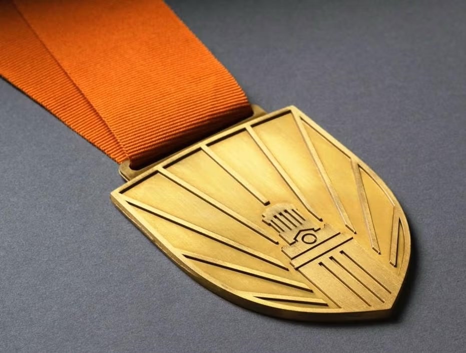 A gold medallion hangs from a burnt-orange ribbon and depicts the UT Tower with rays emanating fro it.