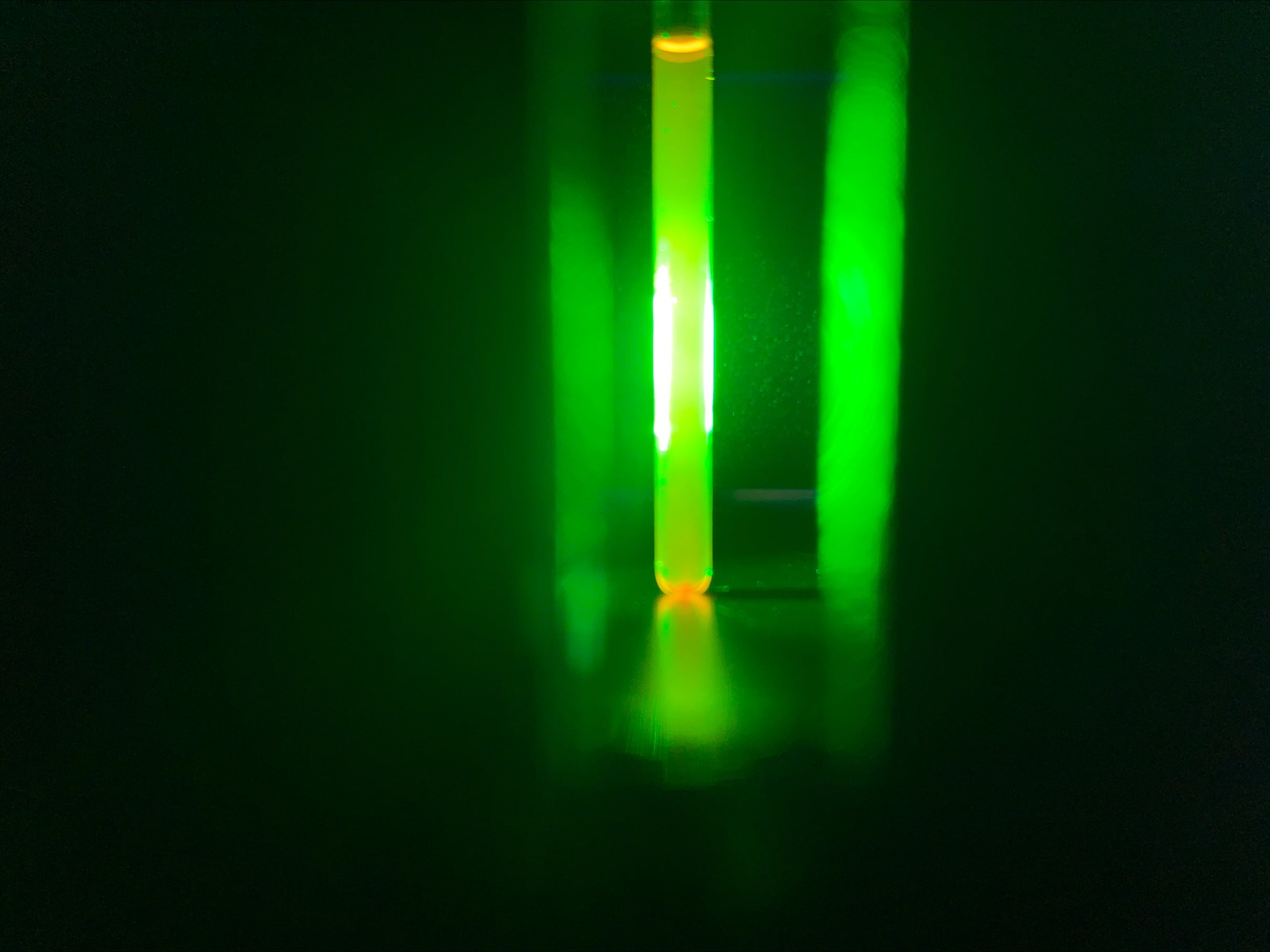 A vial of dye glows green against a black background
