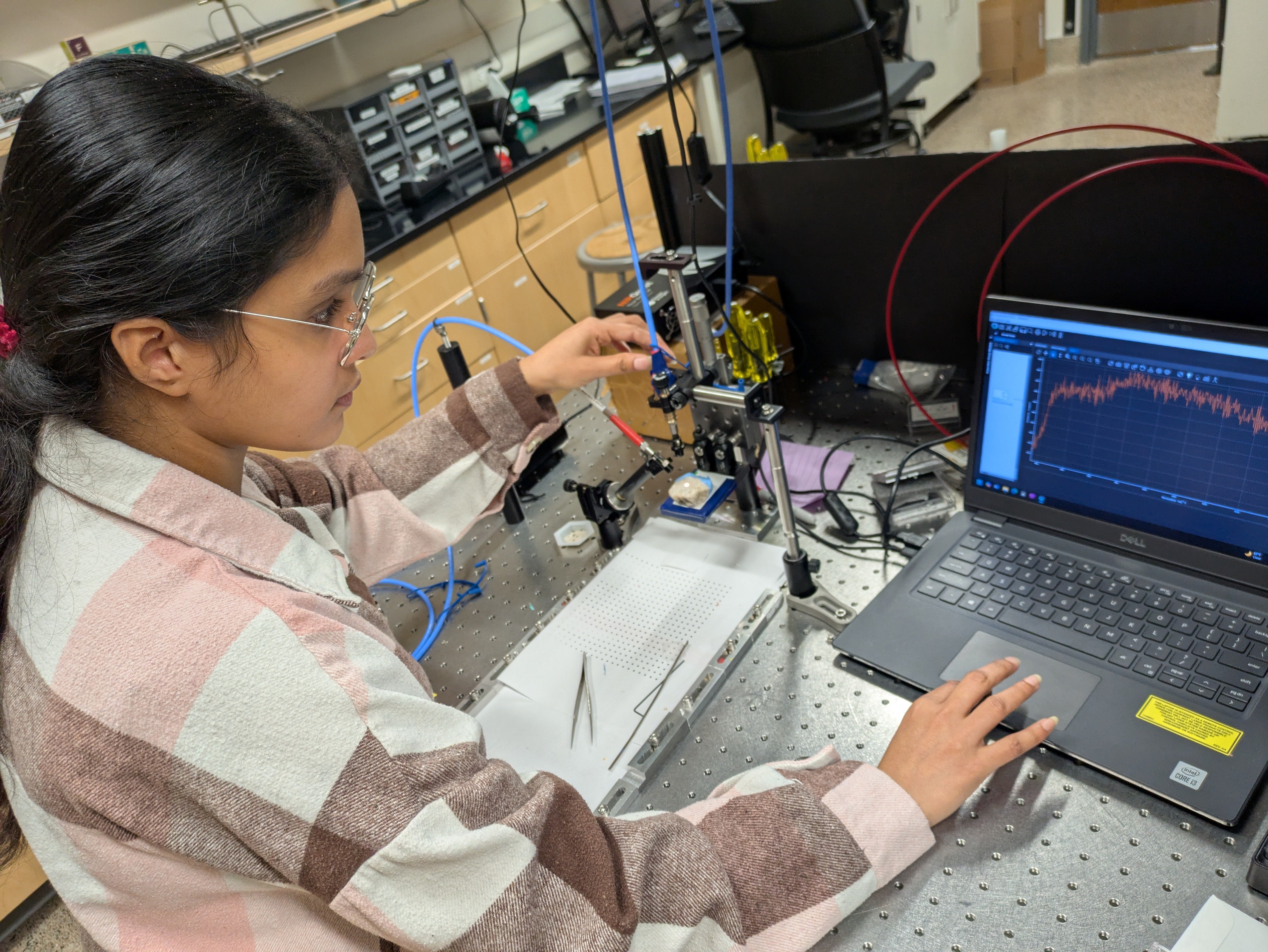 A graduate student at work in the lab with a spectrometer and microplastic sample