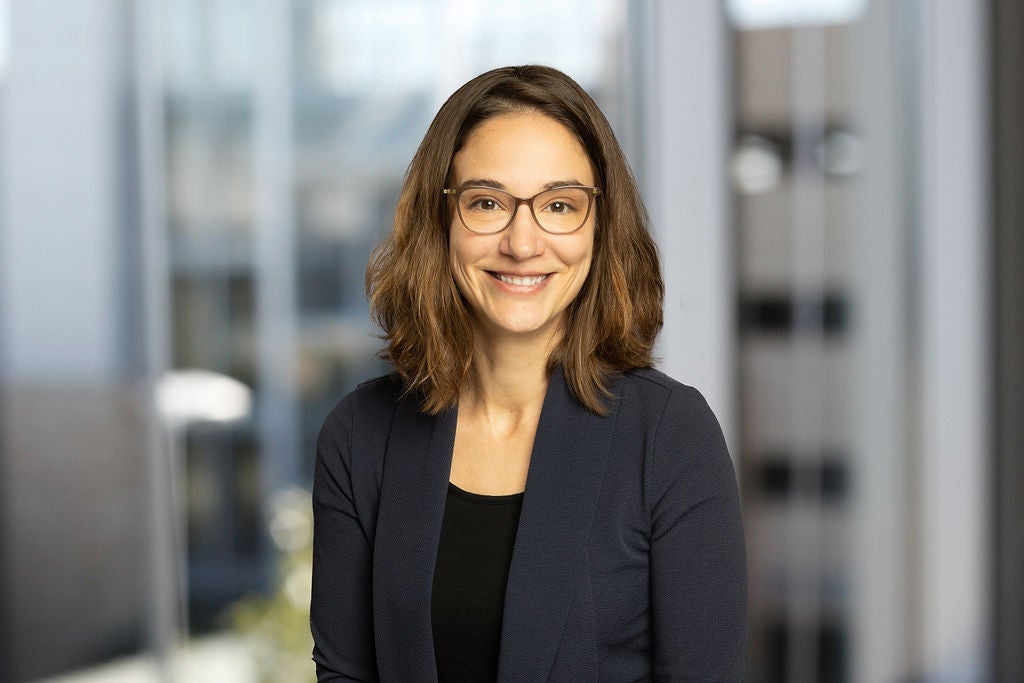 A woman in a suit and glasses stands in front of a glass-paned wall