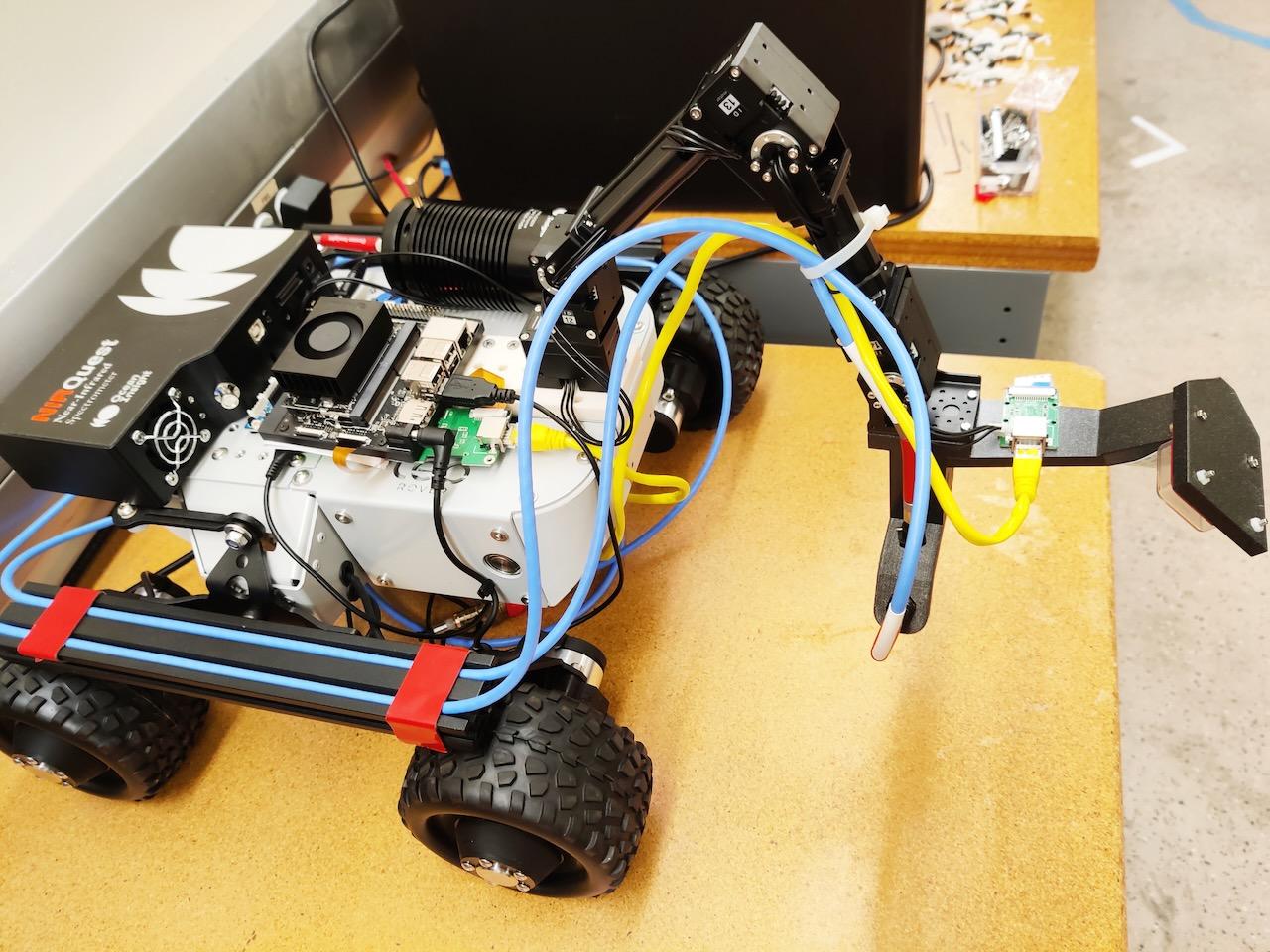 A four-wheeled robot on a desk like surface has tubes and a near-infrared spectrometer labeled NIR QUEST.