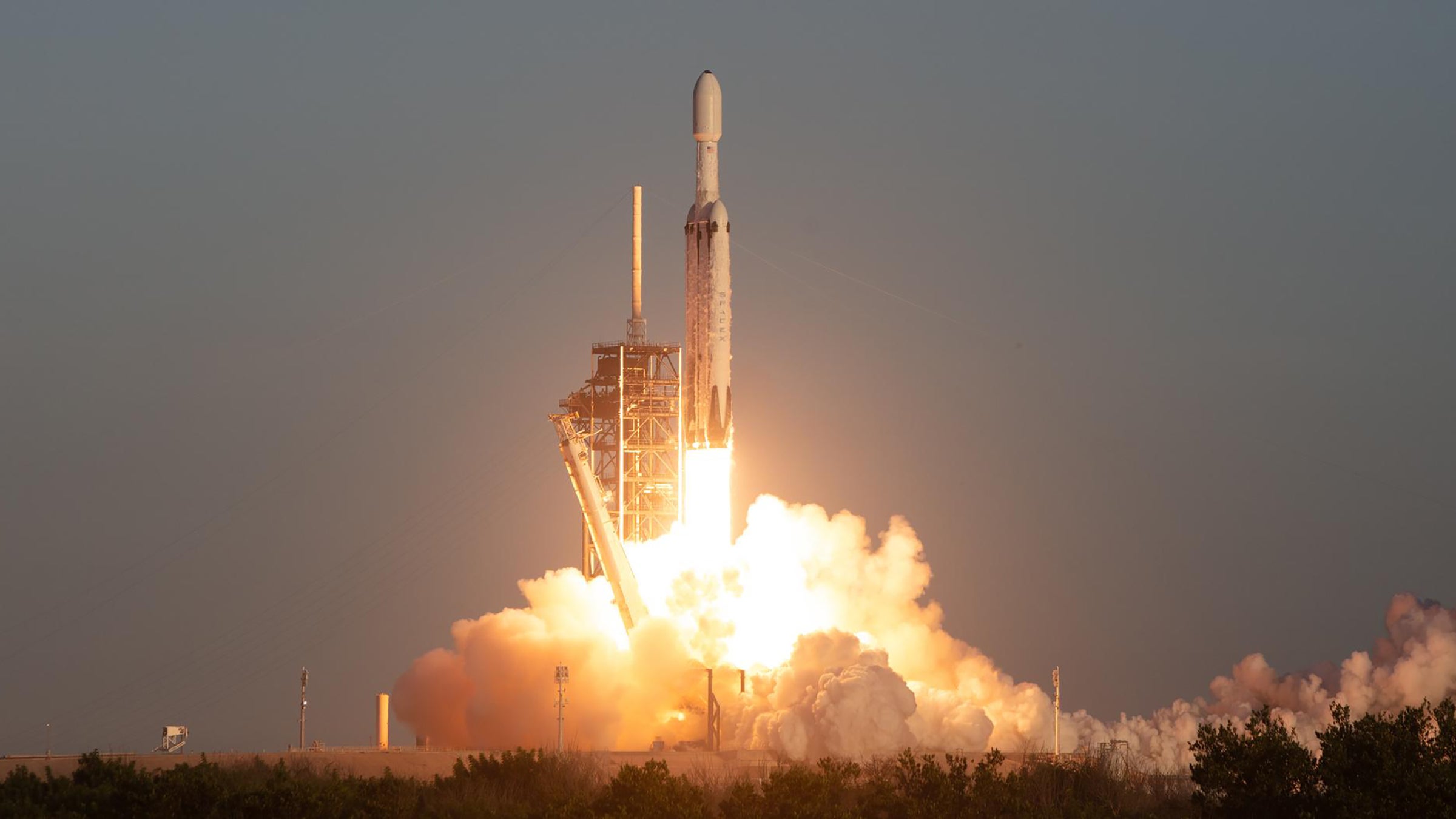 A large rocket launches from a launchpad, trailed by a fiery cloud of smoke