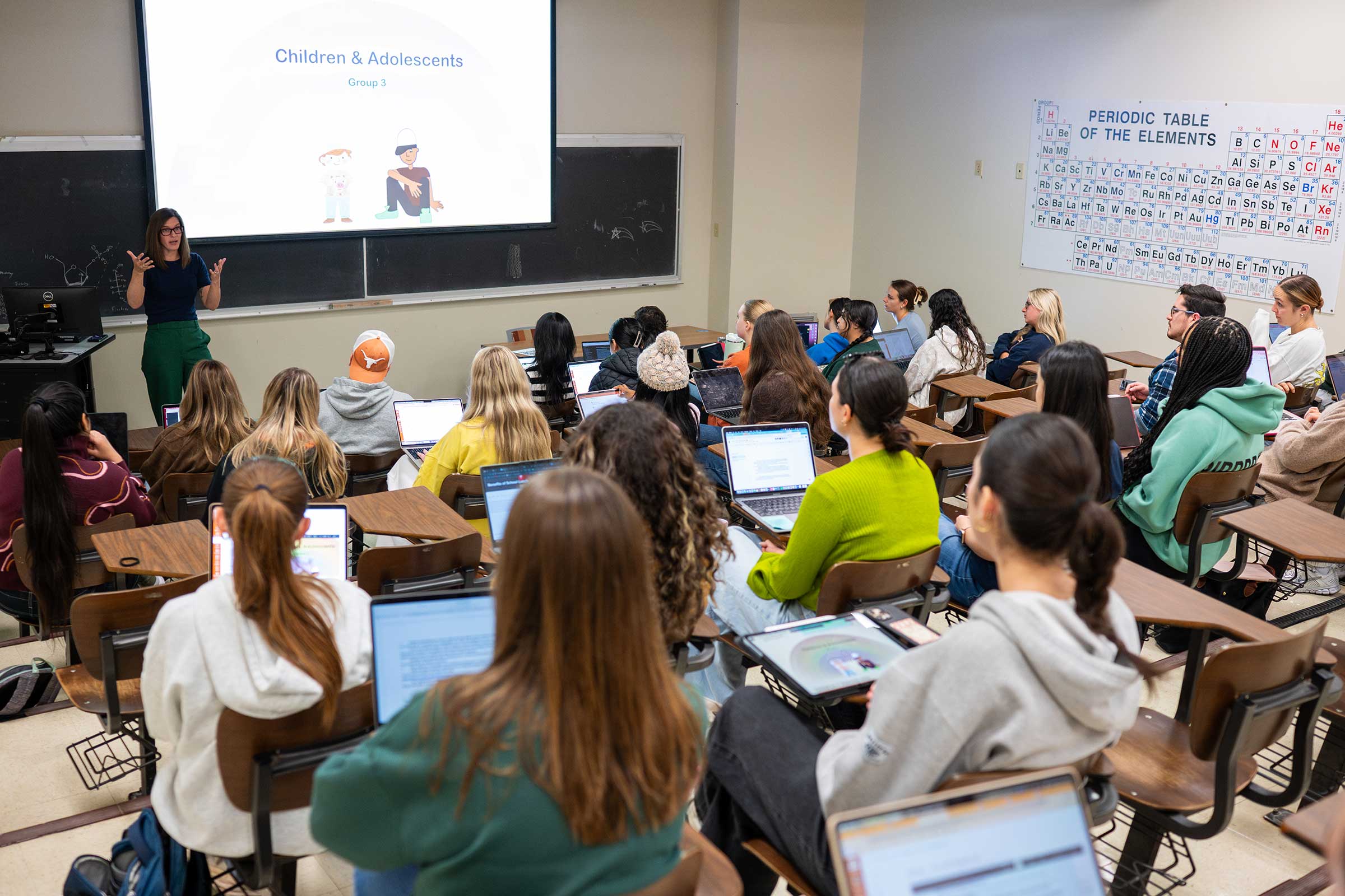 Students in a class learn about children and adolescents as a lecturer projects on a screen and gestures
