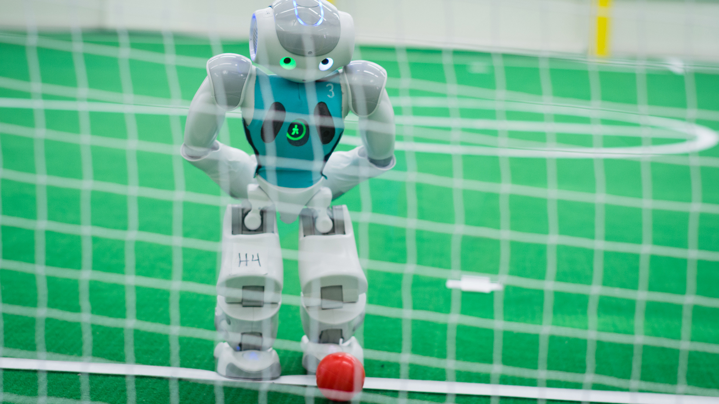 Robot standing on a soccer pitch preparing to kick a red ball into a net