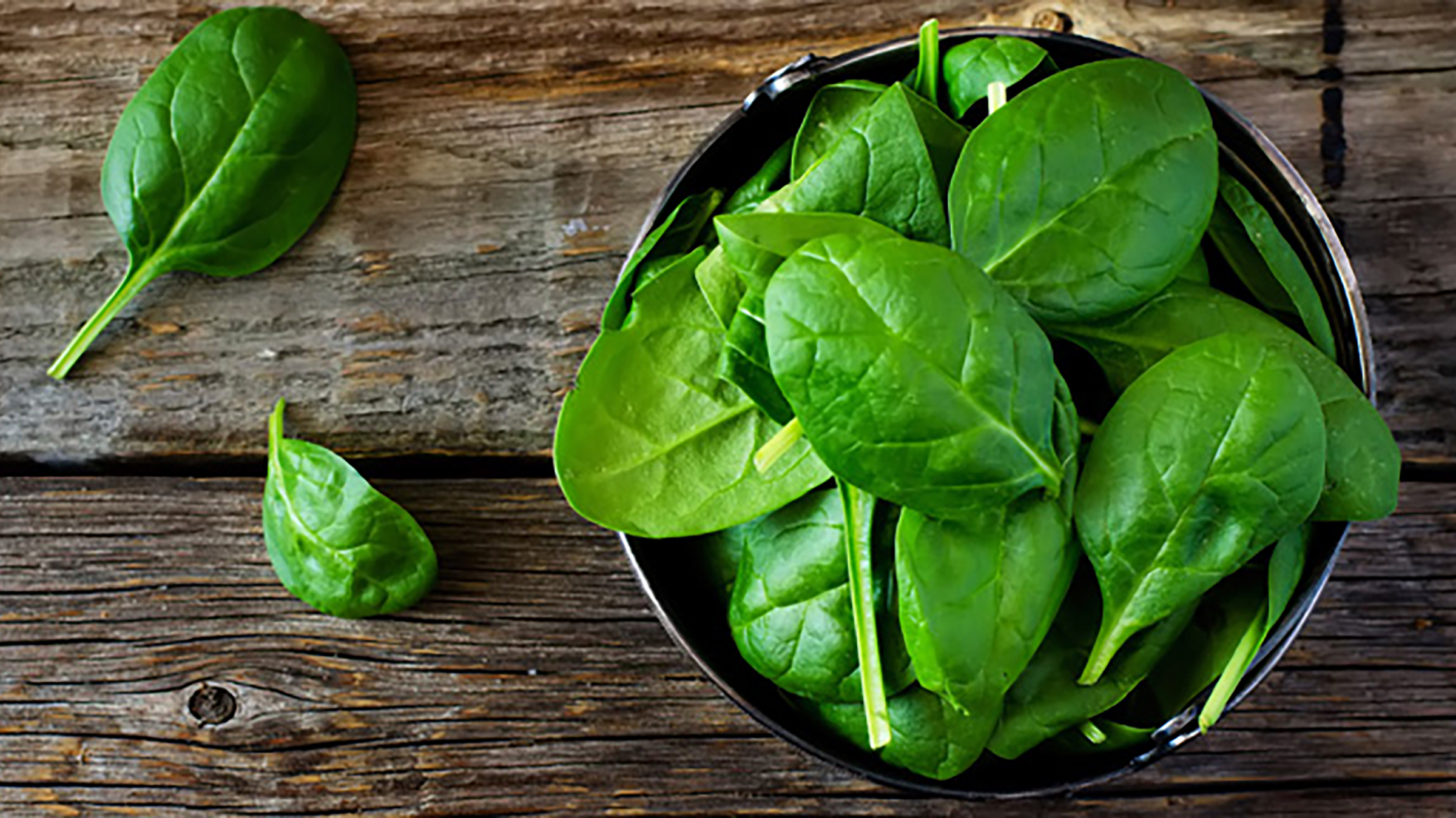 Spinach leaves in a bowl, sitting on a wooden table