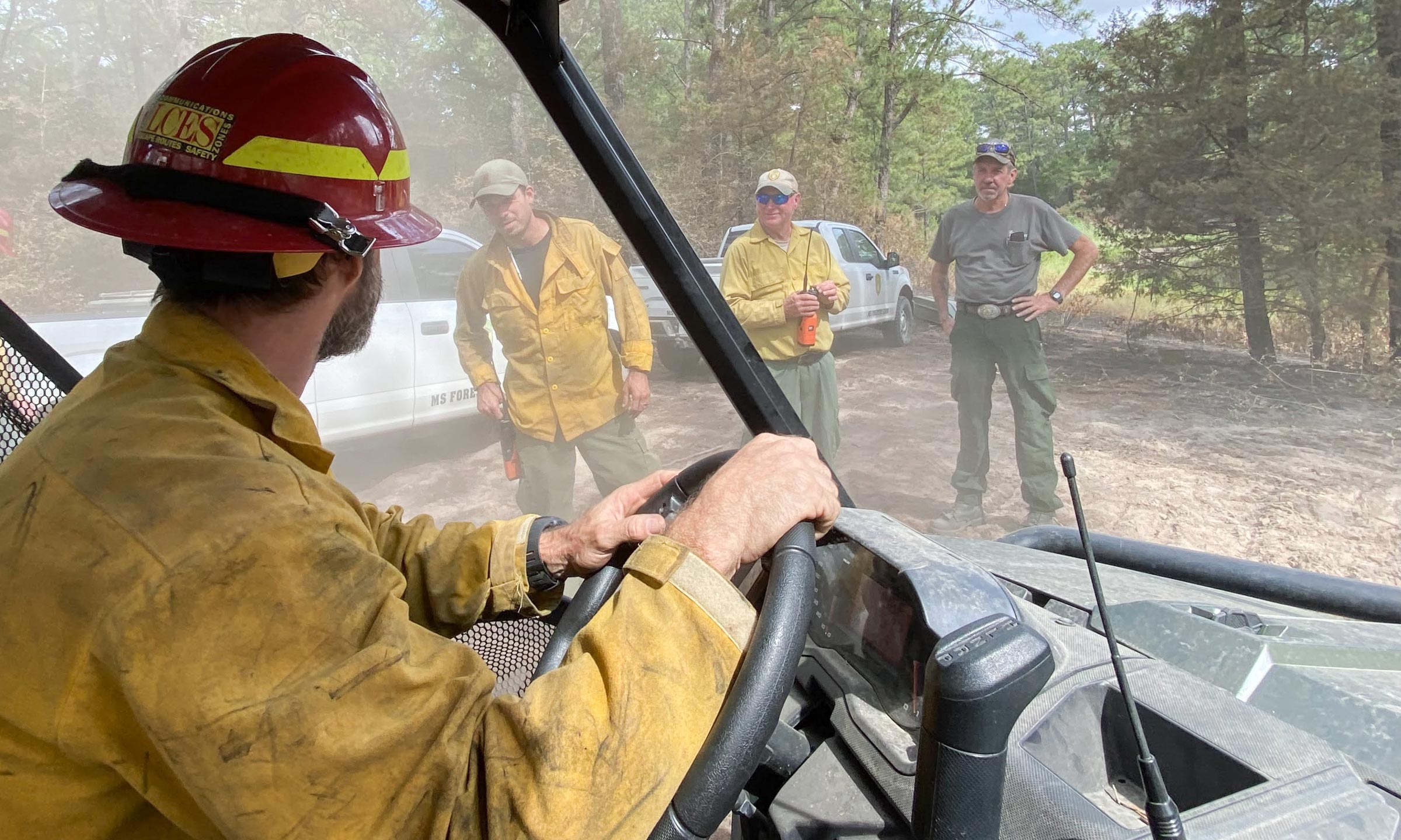 Firefighter at wheel of vehicle consults with colleagues outdoors