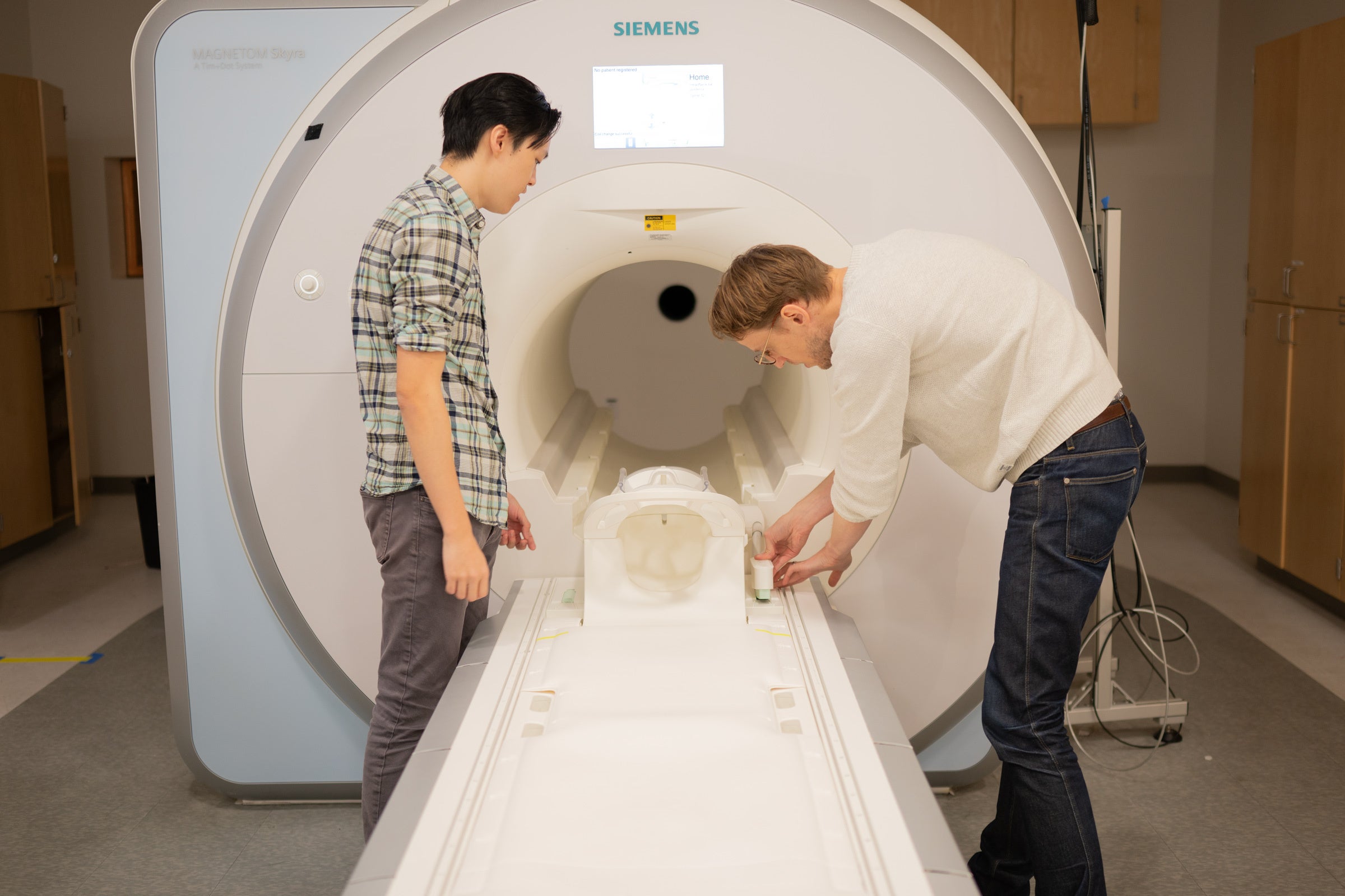 Two scientists prepare an fMRI scanner, a large white cylinder designed to surround a human head
