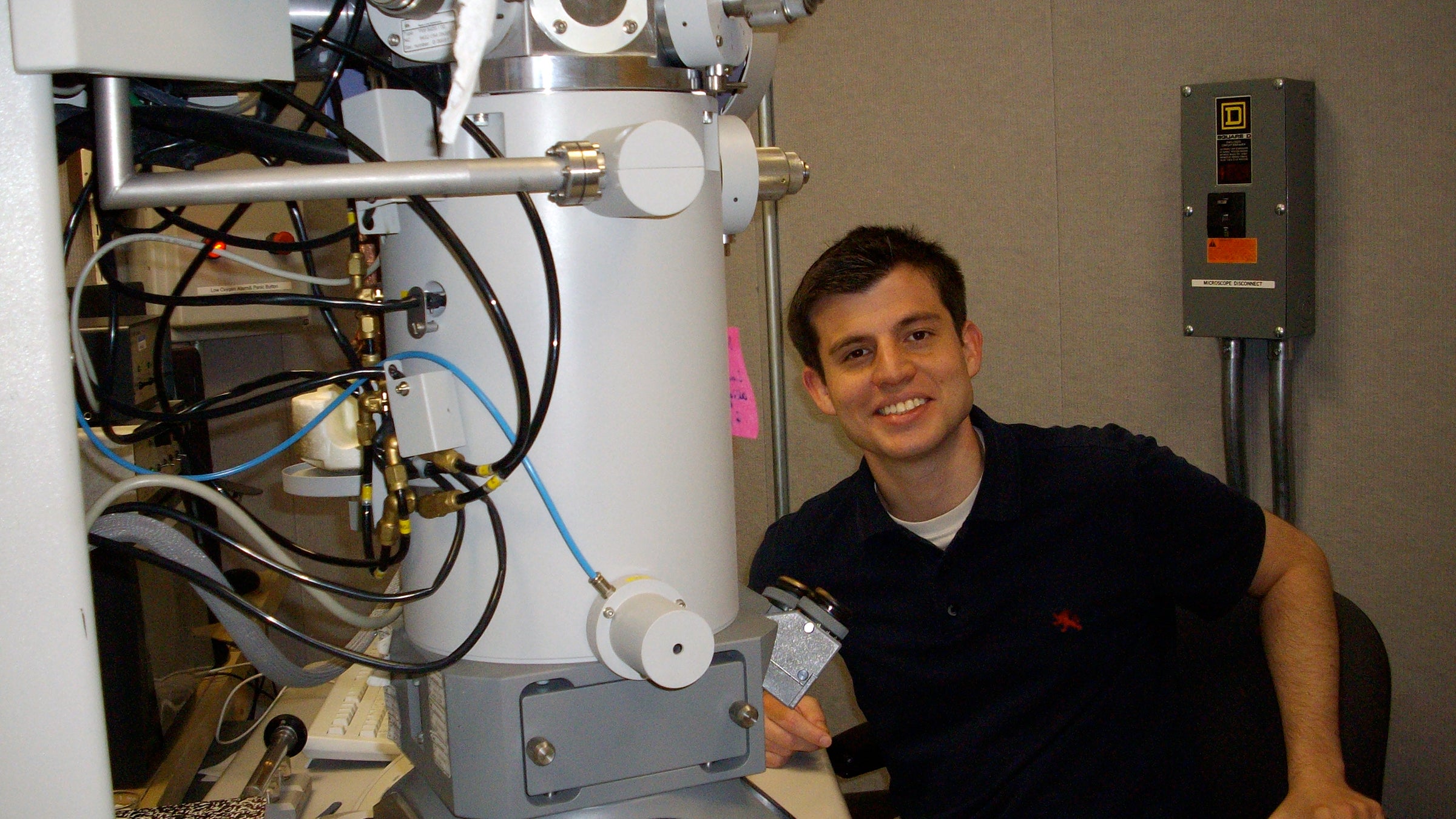 A man sits in front of a large microscope