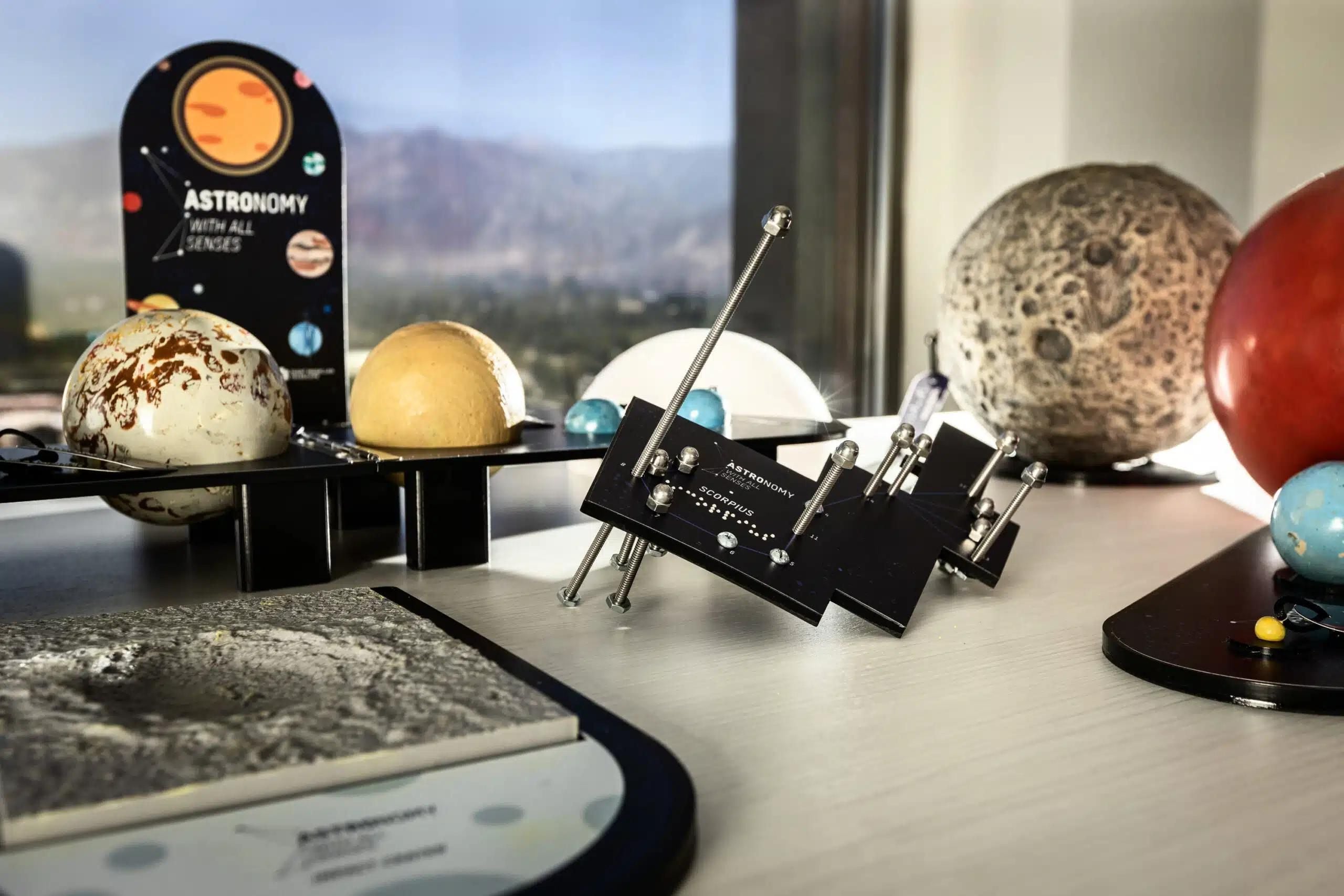 Several small models of planets sit on a desk next to a window