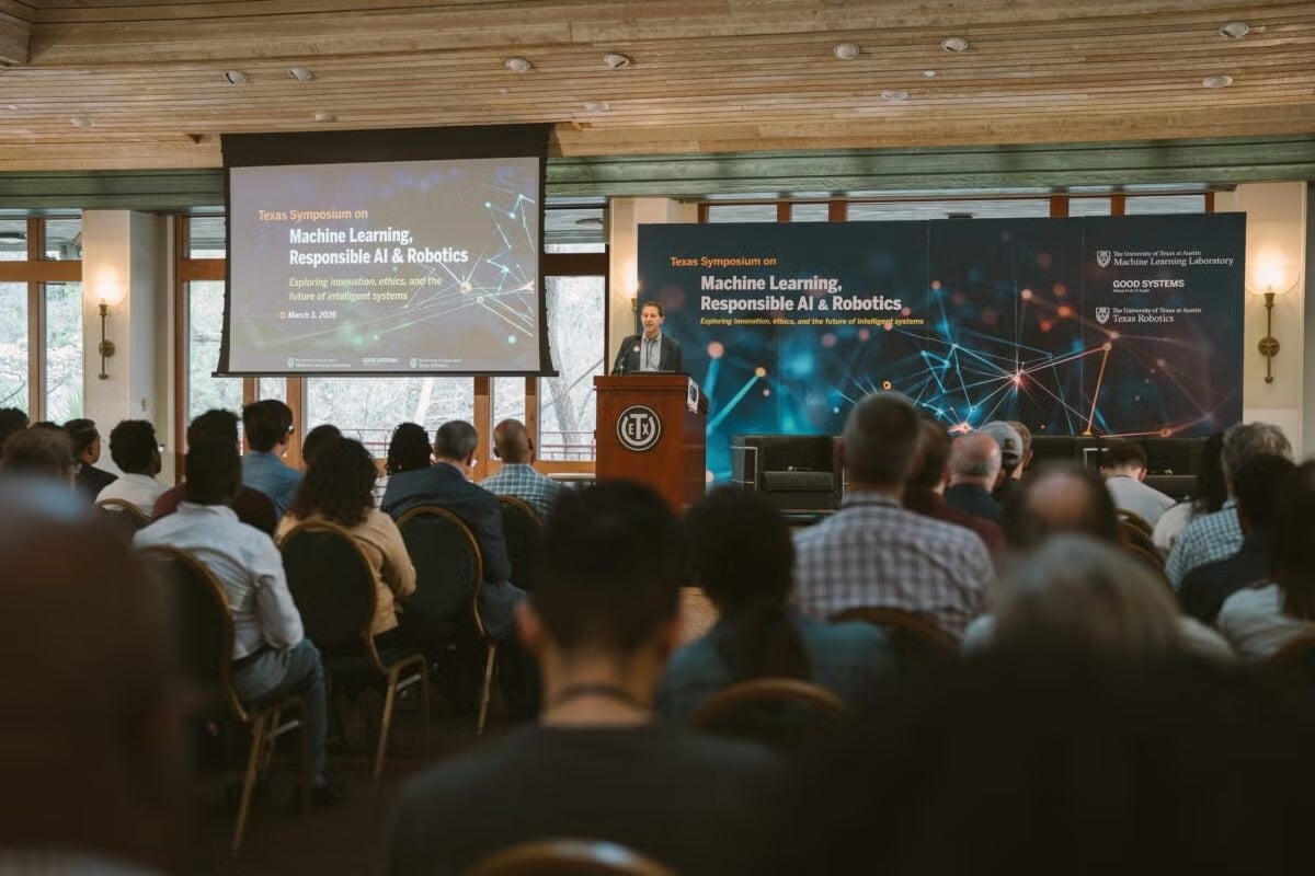 A man at a podium addresses a group of people in rows, while a backsplash behind him and screen state the event name: Texas Symposium on Machine Learning, Responsible Ai & Robotics.