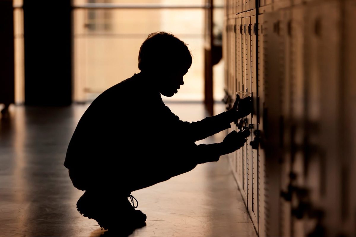 A young person in the shadows of a school hallway at the lockers