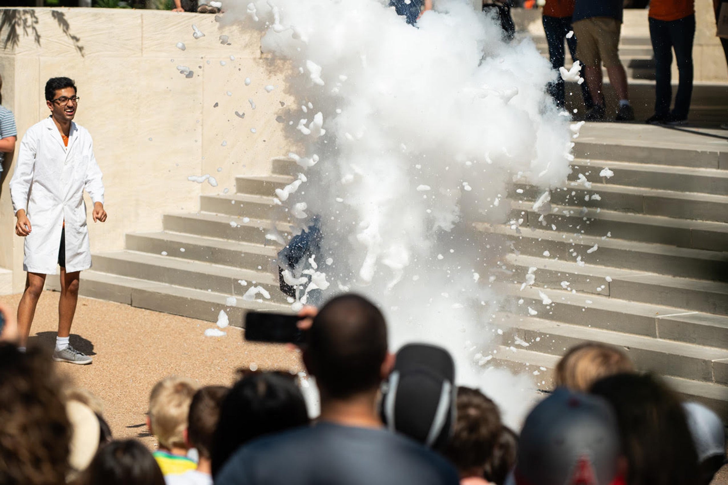 A cloud of nitrogen gas bubbles up in front of a crowd of onlookers and a scientist in a white lab coat.