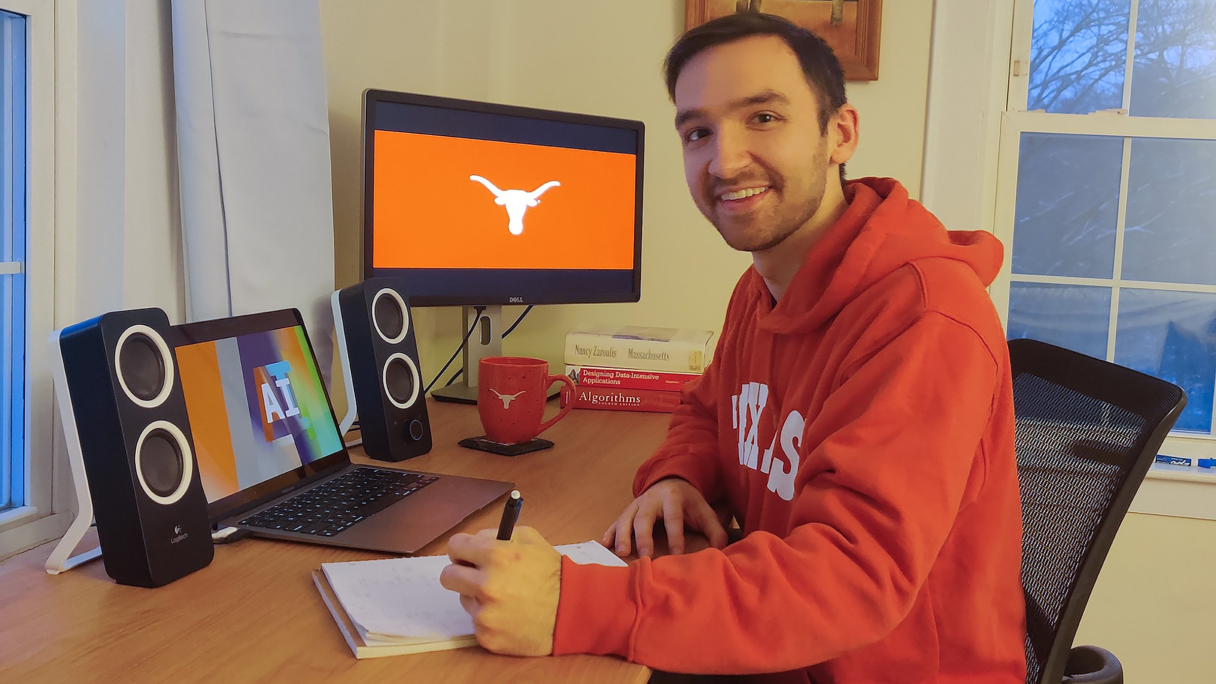 A student wearing a UT sweatshirt sits at a desk with Essentials of AI and a Longhorn silhouette displayed on two screens
