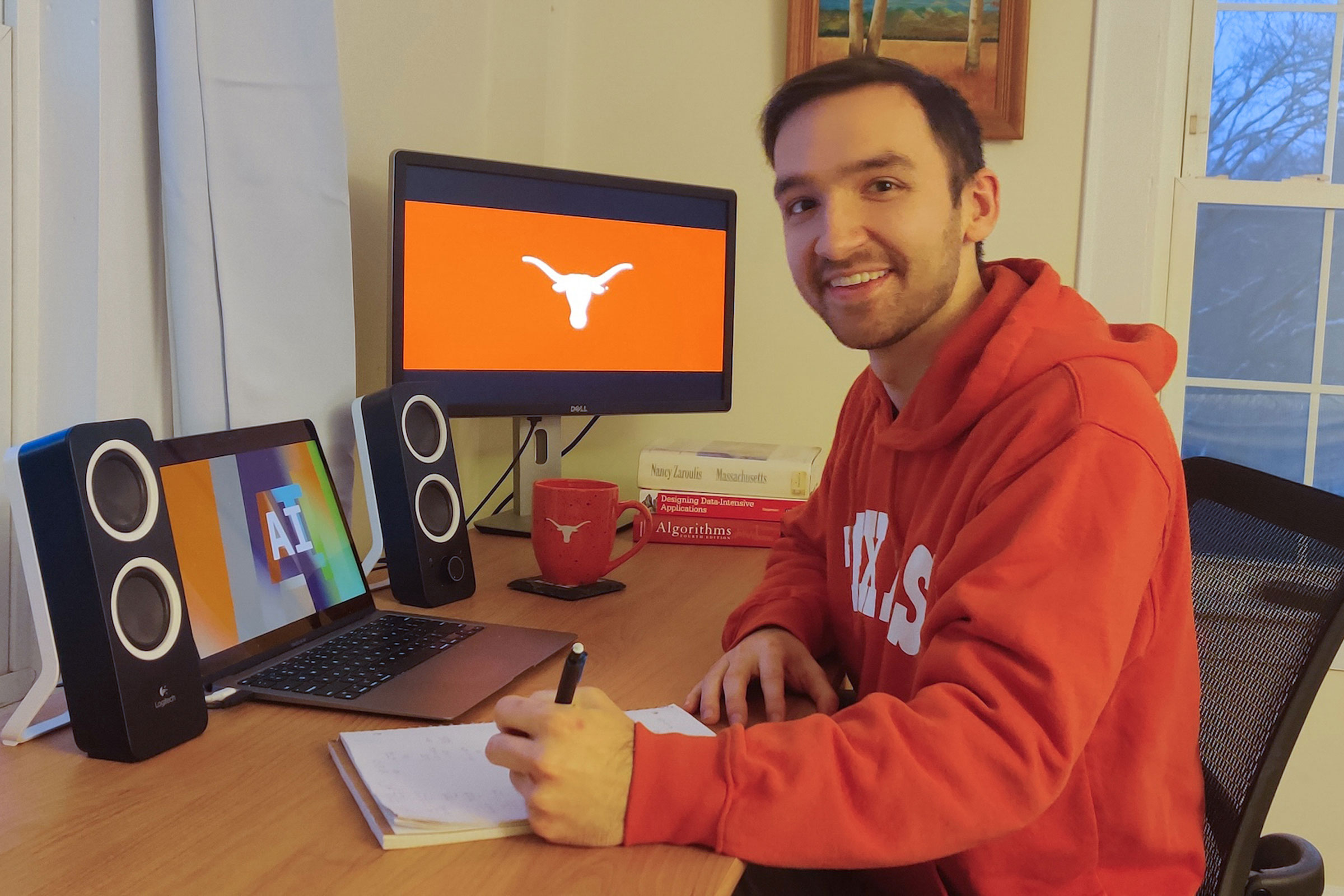 A student wearing a UT sweatshirt sits at a desk with Essentials of AI and a Longhorn silhouette displayed on two screens