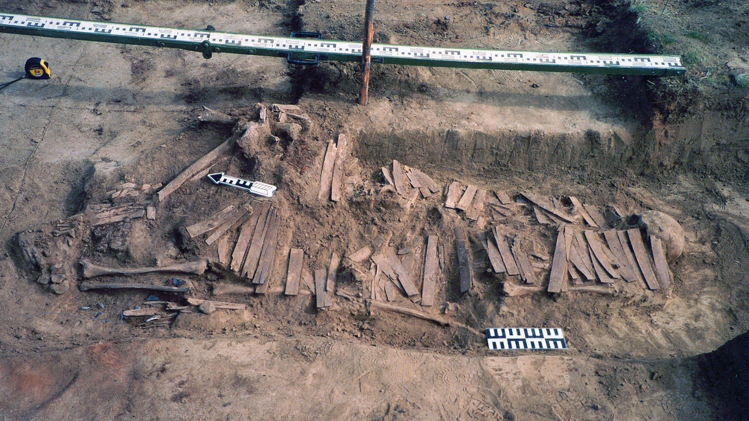 An archaeological dig reveals a burial site with human bones and a series of rectangular armor plates made from animal bone.